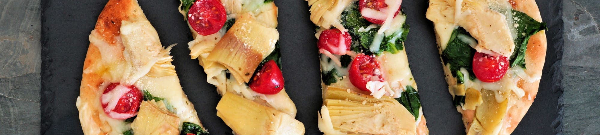 Flat bread pizza with melted mozzarella, tomatoes, spinach and artichokes